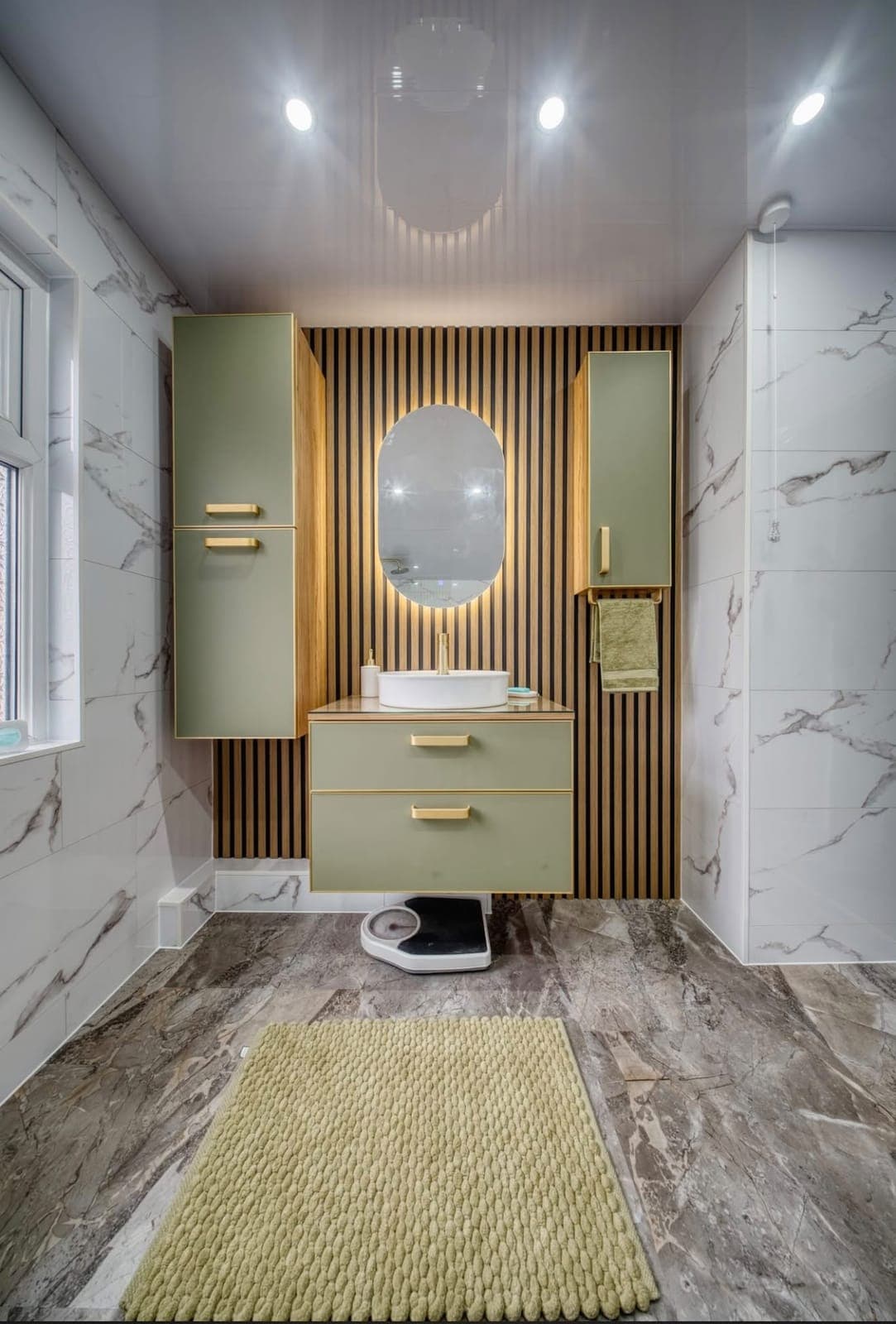 Bathroom with sage green wall cabinets, oak slat panelling and round mirror