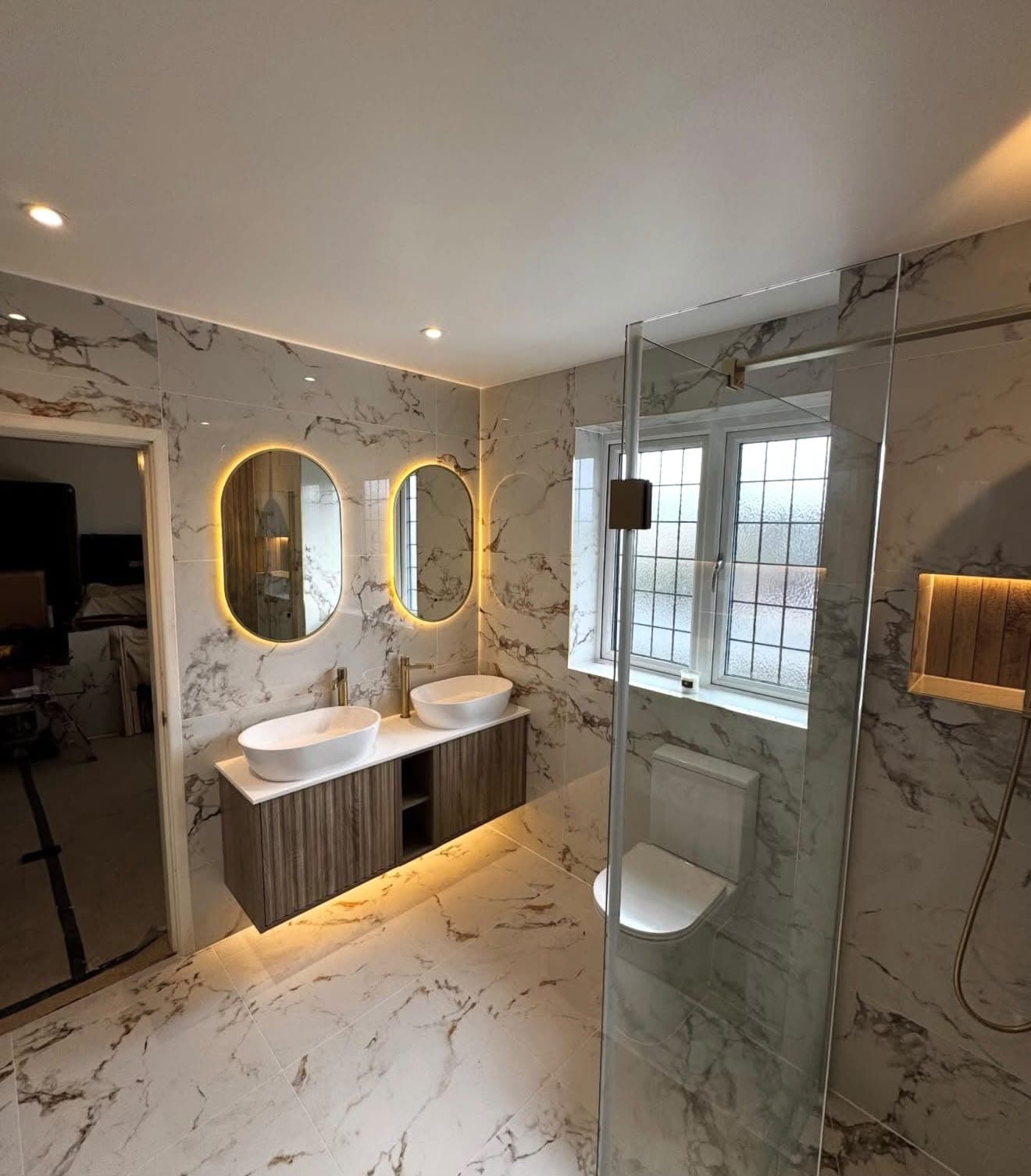Bathroom with twin oval mirrors, illuminated wall-hung vanity and glass shower