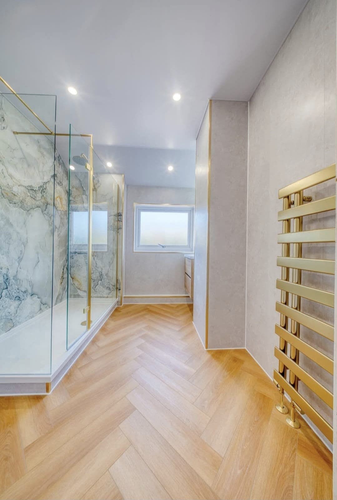Walk-in shower with marble-effect tiles and gold heated towel rail on a herringbone floor