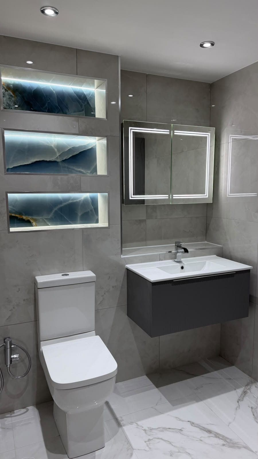 Grey tiled bathroom with wall-hung vanity, illuminated wall niches and mirror cabinet